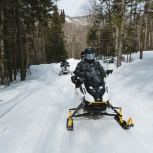 Deux motoneiges Ski-Doo en pleine vitesse sur un sentier bordé de forêt enneigée